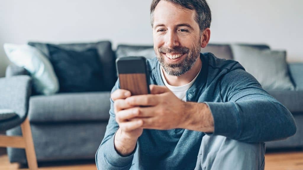 happy man browsing phone in front of couch
