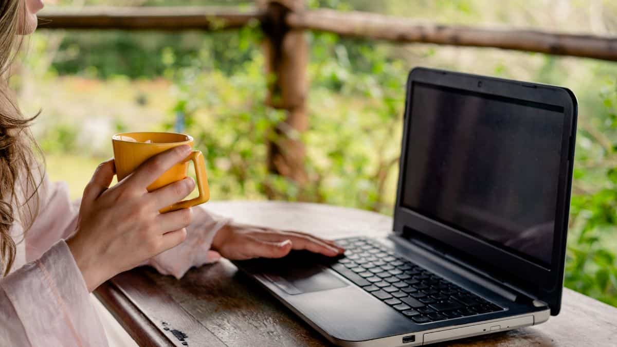 woman using laptop outside holding yellow mug