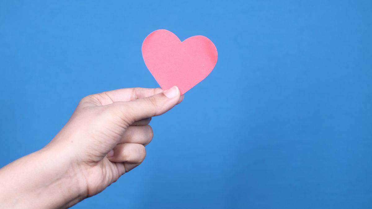 hand holding paper heart against blue background